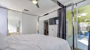 Une chambre dotée d’un grand lit, d’un ventilateur de plafond et d’une porte-fenêtre coulissante donnant sur un balcon avec des sièges d’extérieur.