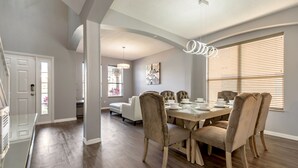 Un coin repas avec une table en bois, des chaises recouvertes d’un tissu beige et un luminaire suspendu moderne.