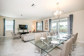 A spacious living room with a glass dining table, a sofa, and a TV.