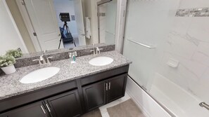 A bathroom with two sinks, dark cabinets, a mirror, and a shower area. - 4815 Crusoe Street (Kissimmee)