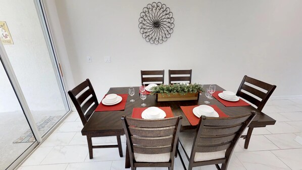 A dining table set for six with red placemats, white plates, and a centerpiece.
