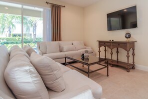 A living room with a beige sofa, a glass coffee table, and a wooden side table with a globe. - 7603 Brookhurst Lane (Kissimmee)