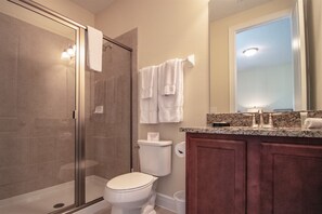 A bathroom with a glass-enclosed shower, a white toilet, and a vanity with a mirror and countertop. - 7603 Brookhurst Lane (Kissimmee)