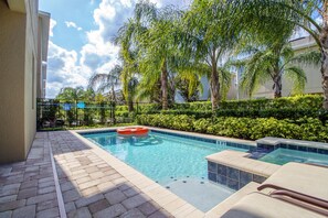 A swimming pool with a floating ring, surrounded by palm trees and a hedge. - 7603 Brookhurst Lane (Kissimmee)