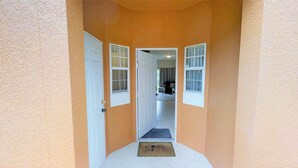 A hallway with a door leading to a room, a window with curtains, and a doormat at the entrance. - 8523 Crystal Cove Loop (Kissimmee)