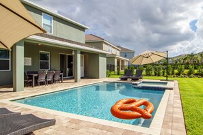 Piscina com espreguiçadeiras e guarda-sóis, cercada por uma casa com área de varanda.