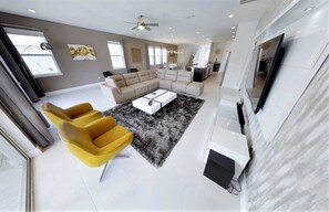 A spacious living area with a sofa, yellow armchairs, a coffee table, and a large TV. - 7736 Graben St (Kissimmee)