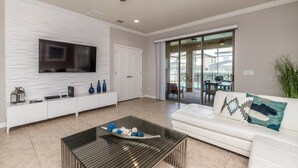 A modern living room with a flat-screen TV, white sofa, and a glass coffee table. - 2105 Morocco Way (Kissimmee)