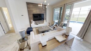 Una sala moderna con un televisor de pantalla plana, un sofá, una mesa de centro y una mesa de comedor de vidrio.