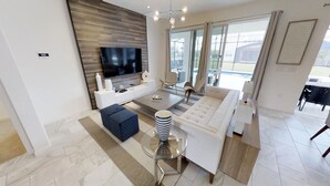 Una sala de estar moderna con un televisor de pantalla plana, un sofá, una mesa de centro y una mesita auxiliar de vidrio.