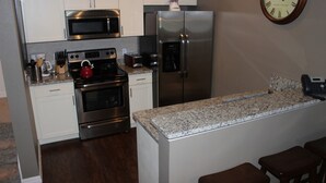 A kitchen with stainless steel appliances, a microwave, a refrigerator, a clock, and a granite countertop.