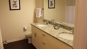 A bathroom with two sinks, a toilet, and framed pictures on the walls.