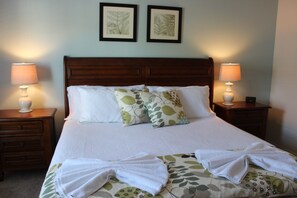 Una cama bien tendida con sábanas blancas y almohadones decorativos, flanqueada por dos mesitas de noche con lámparas.