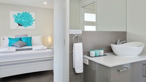 Habitació d'hotel moderna amb un llit, un mirall gran, un rentapeus blanc i una obra d'art color aquamarina a la paret.