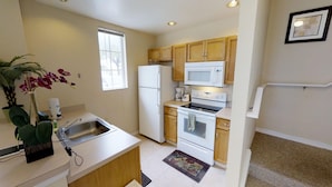 A compact kitchen with a refrigerator, microwave, stove, and sink. - Venetian Bay Villages Four-bedroom (Kissimmee)