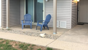 A covered outdoor seating area with two blue chairs and a glass door leading to a balcony. - Cozy Retreat Across from the Clubhouse - 2bd/2ba Condo (Sleeps 6)  (Fraser)
