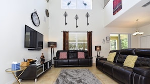 A living room with a black leather sofa, a TV, a fireplace, and a large window with curtains. - Watersong Resort Six-bedroom (Davenport)