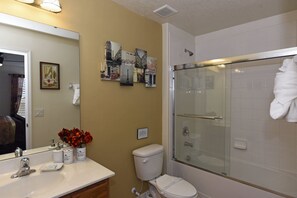Une salle de bain avec un lavabo blanc, des toilettes et une douche en verre. Des tableaux encadrés ornent le mur, et un miroir est placé au-dessus du lavabo.