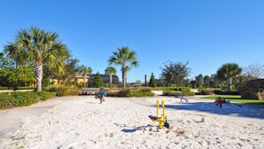 Zona arenosa de playa con juegos infantiles y palmeras.