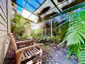 A wooden bench, a pathway, and lush green ferns under a glass roof structure. - Raspberry Terrace | Art Deco Cottage, 3 Bedroom, 1.5 Bathroom, A/C, BBQ, Kiwi Pergola, Near Leura Mall (Leura)