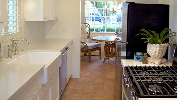 Cocina con armarios blancos, estufa a gas, lavavajillas y comedor con silla y mesa.