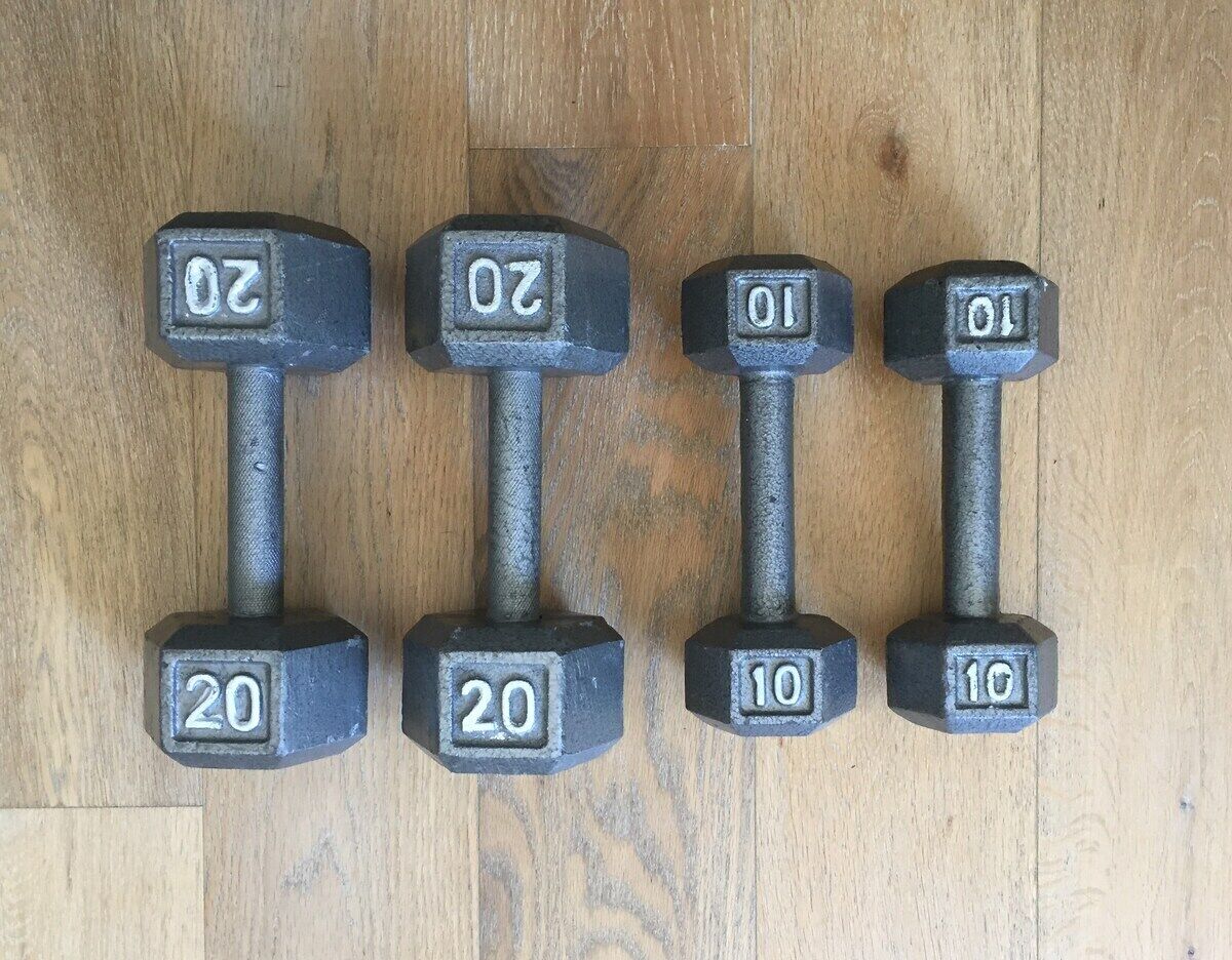 Four dumbbells with weights of 20 and 10, arranged on a wooden floor.