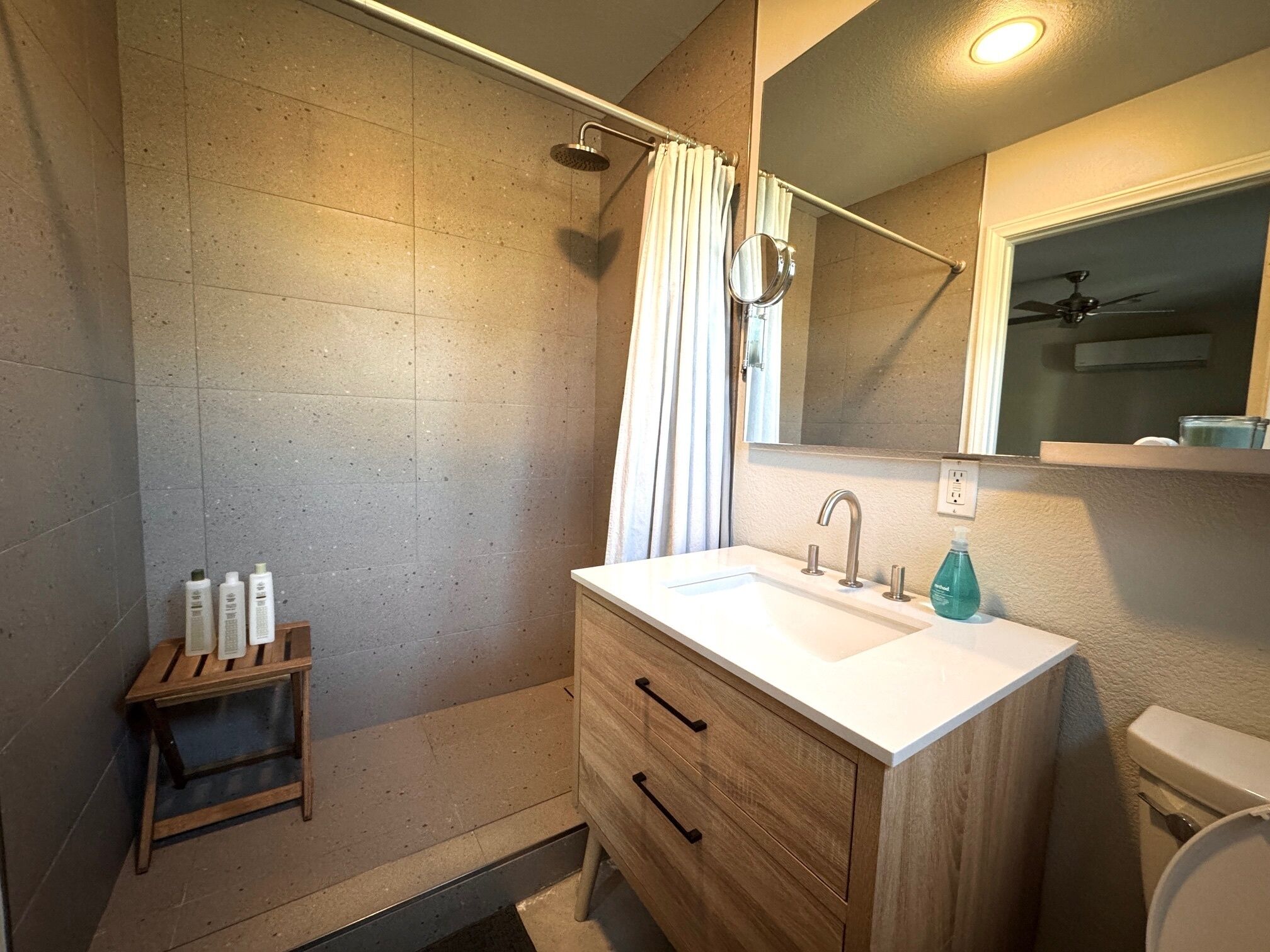 Un baño moderno con ducha, tocador con espejo y artículos de aseo sobre una mesita.