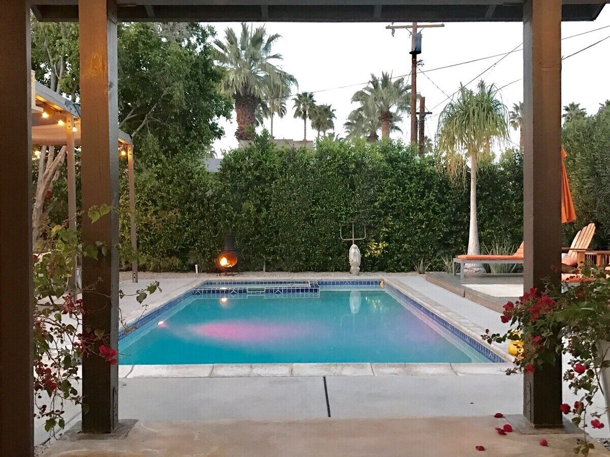 A rectangular pool with a tiled edge, surrounded by a concrete deck. There are lounge chairs and a tiki torch visible in the background.