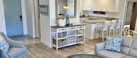 A modern living room with a coffee table, two sofas, a dining area with white chairs, and a kitchen with white cabinets.