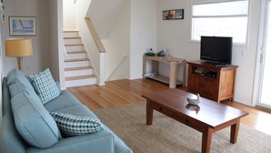 A living room with a sofa, a wooden coffee table, a television, a staircase, and a window. - One House to beach- beach chairs & badges too! (Beach Haven)