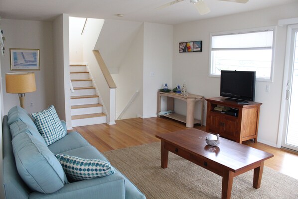 A living room with a sofa, a wooden coffee table, a television, a staircase, and a window.