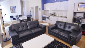A modern living room with two black leather sofas, a white coffee table, and a kitchen area with white cabinets and appliances. - Golf and Beach Retreat (Collingwood Park)