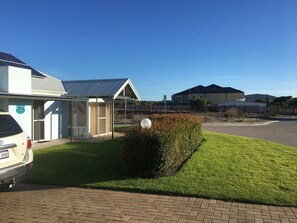 A modern building with a solar panel roof, a covered outdoor seating area, and a paved driveway. - Golf and Beach Retreat (Collingwood Park)