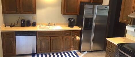 Una cocina con armarios de madera, un refrigerador de acero inoxidable, un lavavajillas y una cafetera.