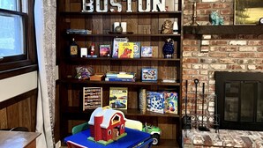 Een gezellige kamer met een boekenkast met de tekst 'BOSTON', een open haard en een kleine tafel met stoelen.