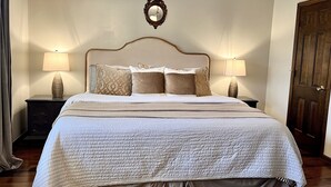 Een net opgemaakt bed met een gewatteerde witte spreideken, twee bedlampjes en een spiegel boven het hoofdeinde.