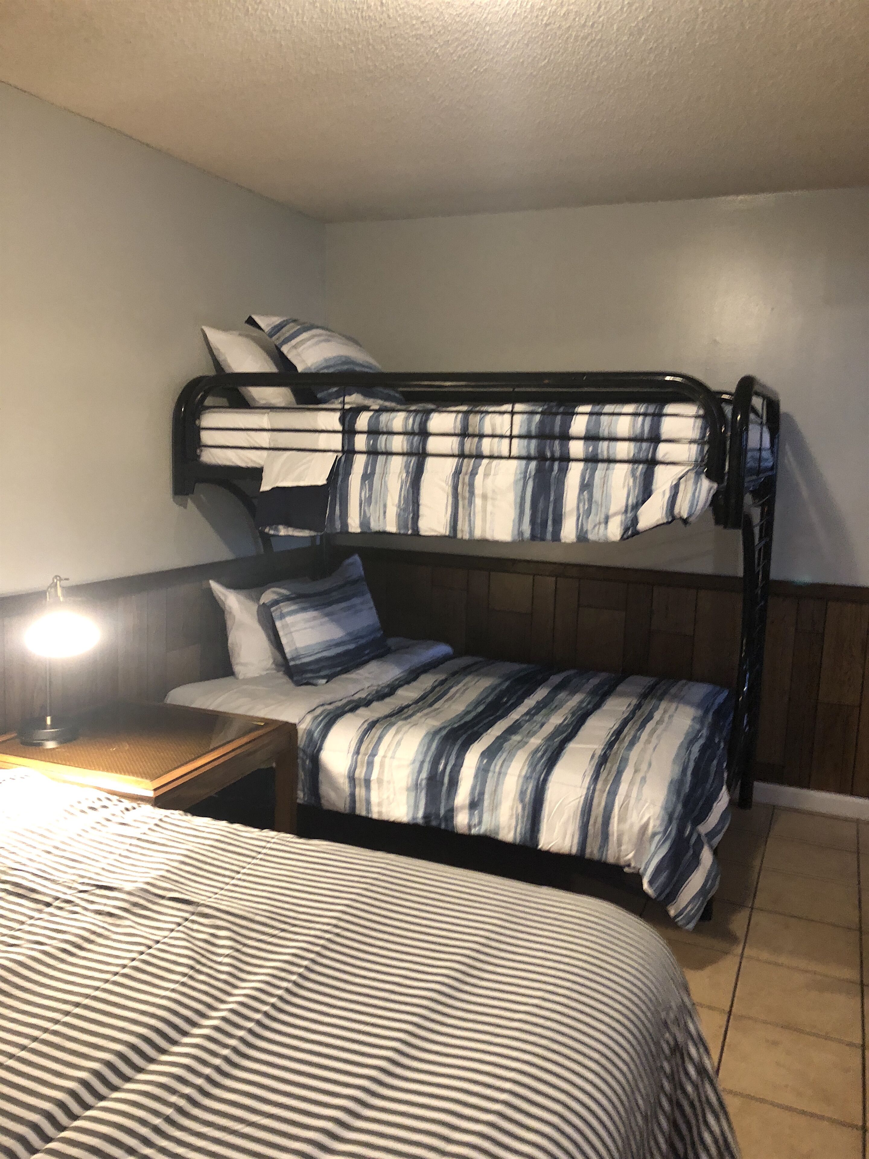 Una cama individual con ropa de cama a rayas, una mesita de noche con lámpara y un cabecero de madera.