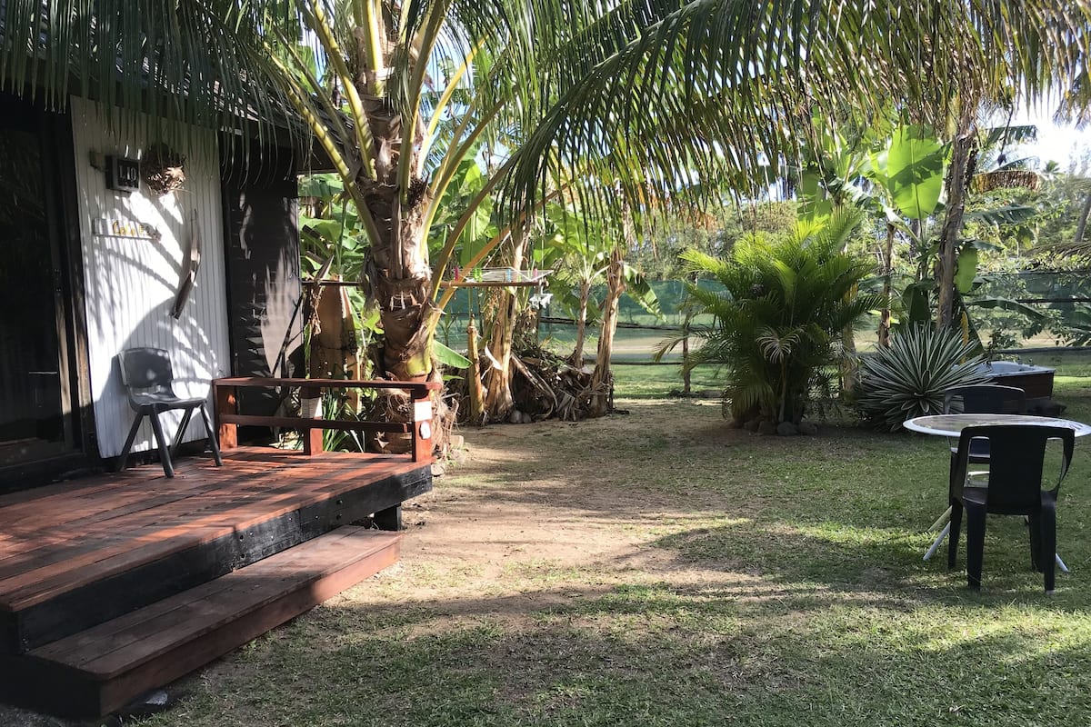 A patio with a wooden deck, outdoor seating, and a variety of tropical plants.
