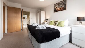 Ein modernes Schlafzimmer mit Bett, Nachttischen, einem Kleiderschrank und einem durchgehenden Türbogen sichtbarem Badezimmer.