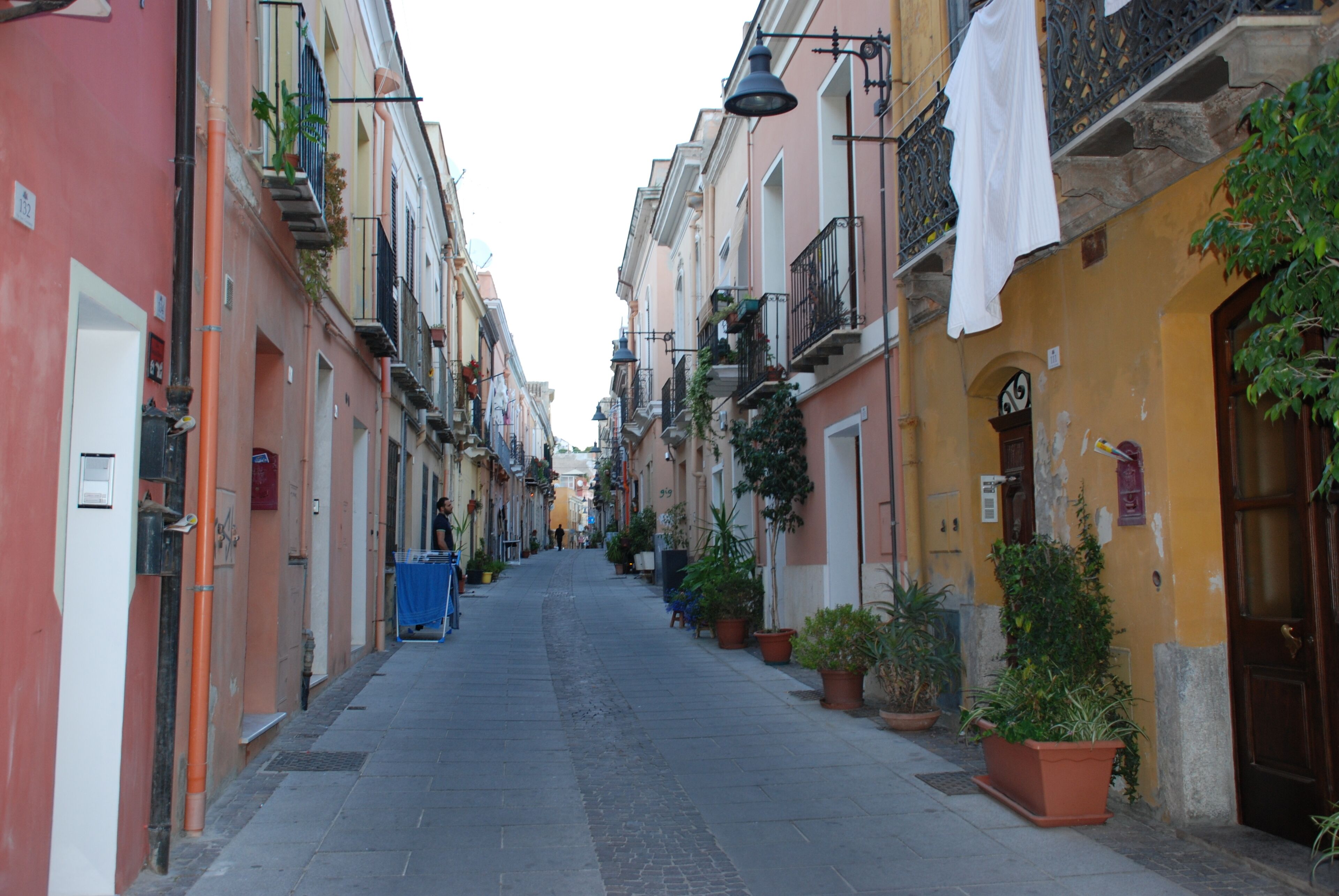 Une rue étroite bordée de bâtiments aux couleurs vives, de plantes en pot et de linge suspendu pour sécher.