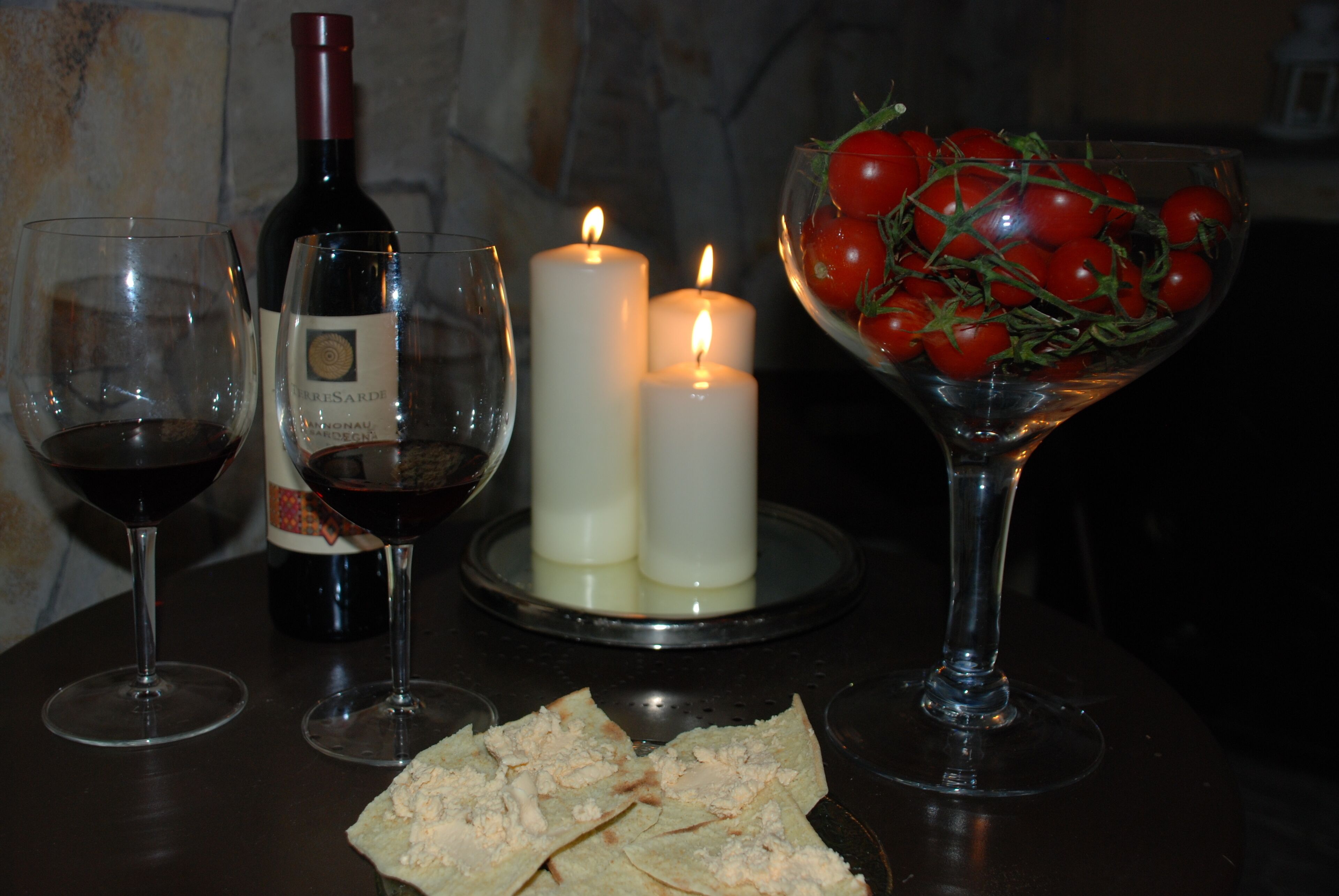 A table with wine glasses, a bottle of wine, candles, and a bowl of cherry tomatoes.