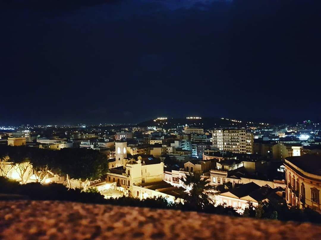A nighttime cityscape with illuminated buildings and a prominent hill in the background.