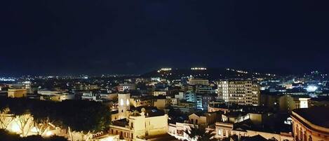 A nighttime cityscape with illuminated buildings and a prominent hill in the background.