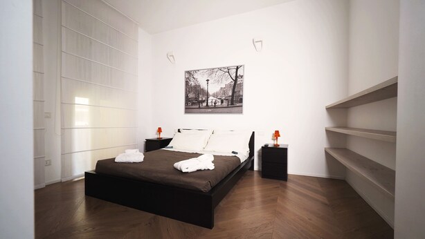 A modern bedroom with a large bed, a nightstand with a lamp, and a wall-mounted shelf. - Luxury appartment in Montenapoleone (120 sqm) with parking in the building (Milano)