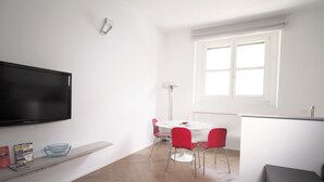 A modern living room with a flat-screen TV, a white dining table with red chairs, and a large window. - Luxury appartment in Montenapoleone (120 sqm) with parking in the building (Milano)