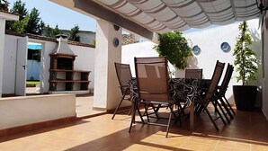 Un patio al aire libre con mesa y sillas, una parrilla y un área cubierta con un toldo a rayas.