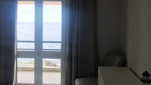 Et hotelværelse med en seng, et lille bord, en lampe og havudsigt gennem et stort vindue.