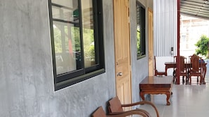 A row of wooden chairs against a wall with large windows and a door. - Baan Saun Homestay by Lamyai Khunmae (Ban Thi)