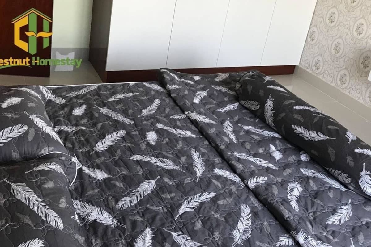A bedroom with a bed featuring a black and white feather pattern bedspread, a wooden headboard, and a white wardrobe with a mirror.