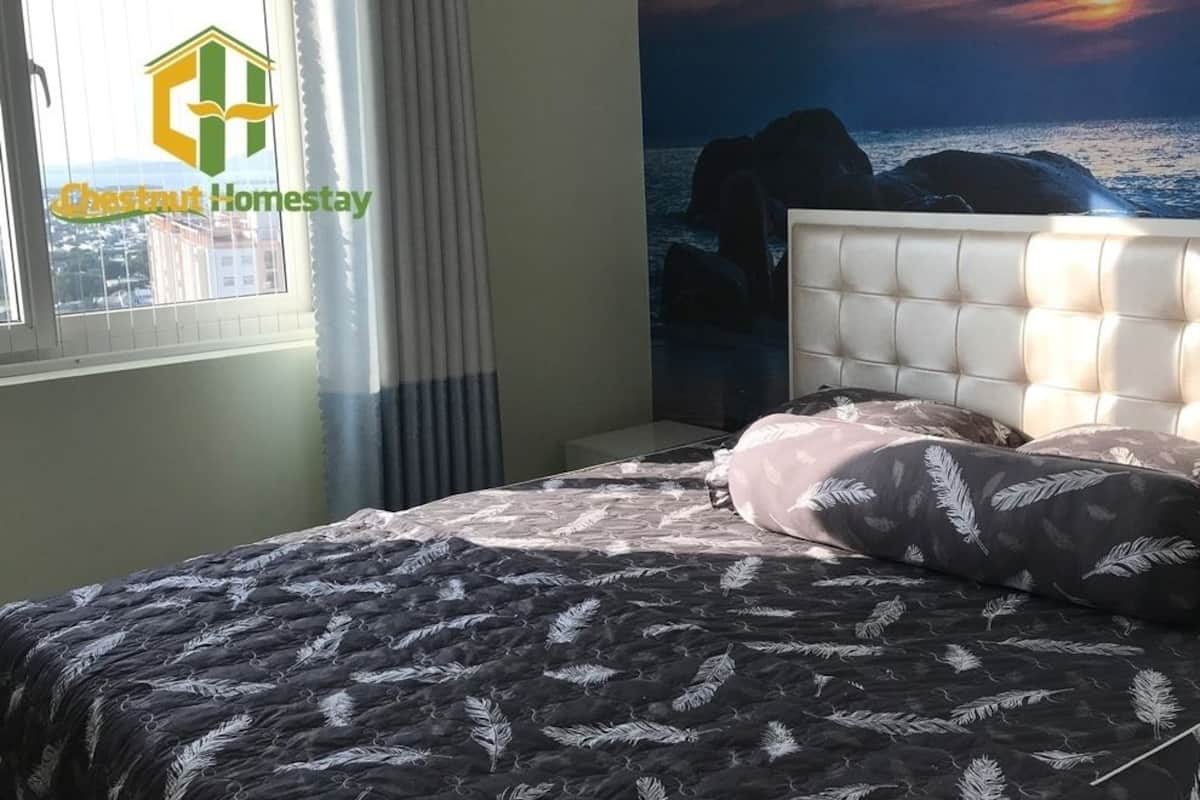 A bedroom with a bed, a headboard, and a view of the sea through a window.